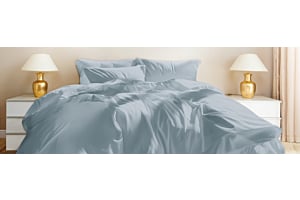 Eine blaue Tencel Bettwäsche auf einem schönen Bett in einem sonnigen Raum. Neben dem Bett stehen goldige Lampen.