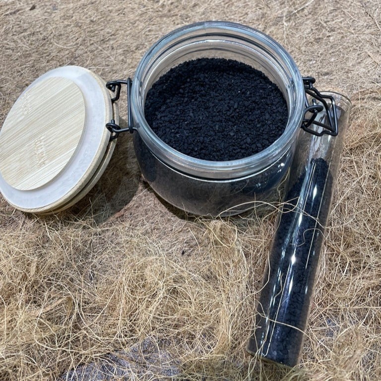 Un bocal de conservation avec des petits grains noirs de charbon actif à l'intérieur, sur un lit de laine décorative. 