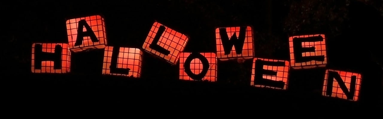 Inscription "Halloween". L'image montre neuf cubes orange sur fond noir, alignés les uns derrière les autres avec un léger décalage. Sur chaque cube se trouve une lettre. Les lettres assemblées forment le mot "Halloween"".