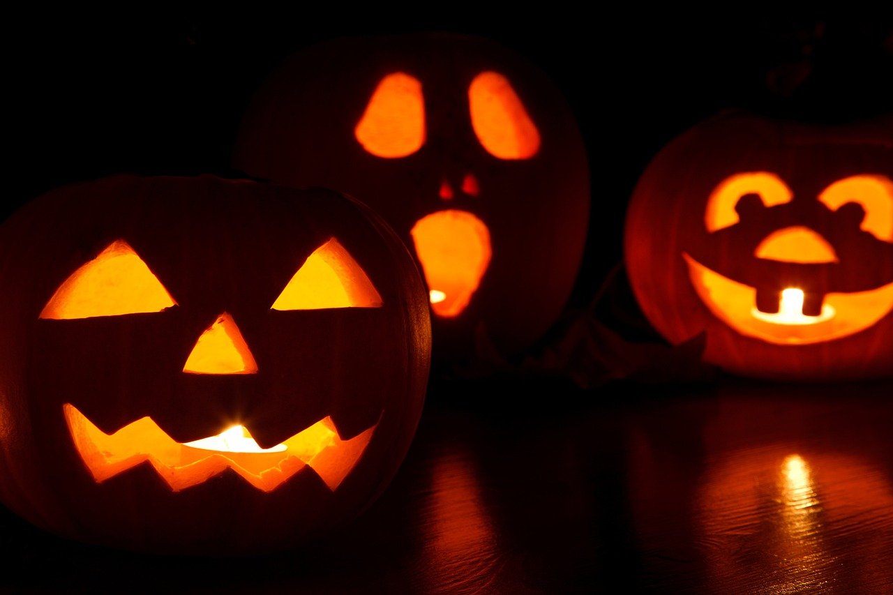 Trois citrouilles d'Halloween avec des grimaces sculptées. L'image montre trois citrouilles d'Halloween sculptées sur un fond sombre, chacune équipée d'une lumière. Chaque citrouille a une grimace différente.